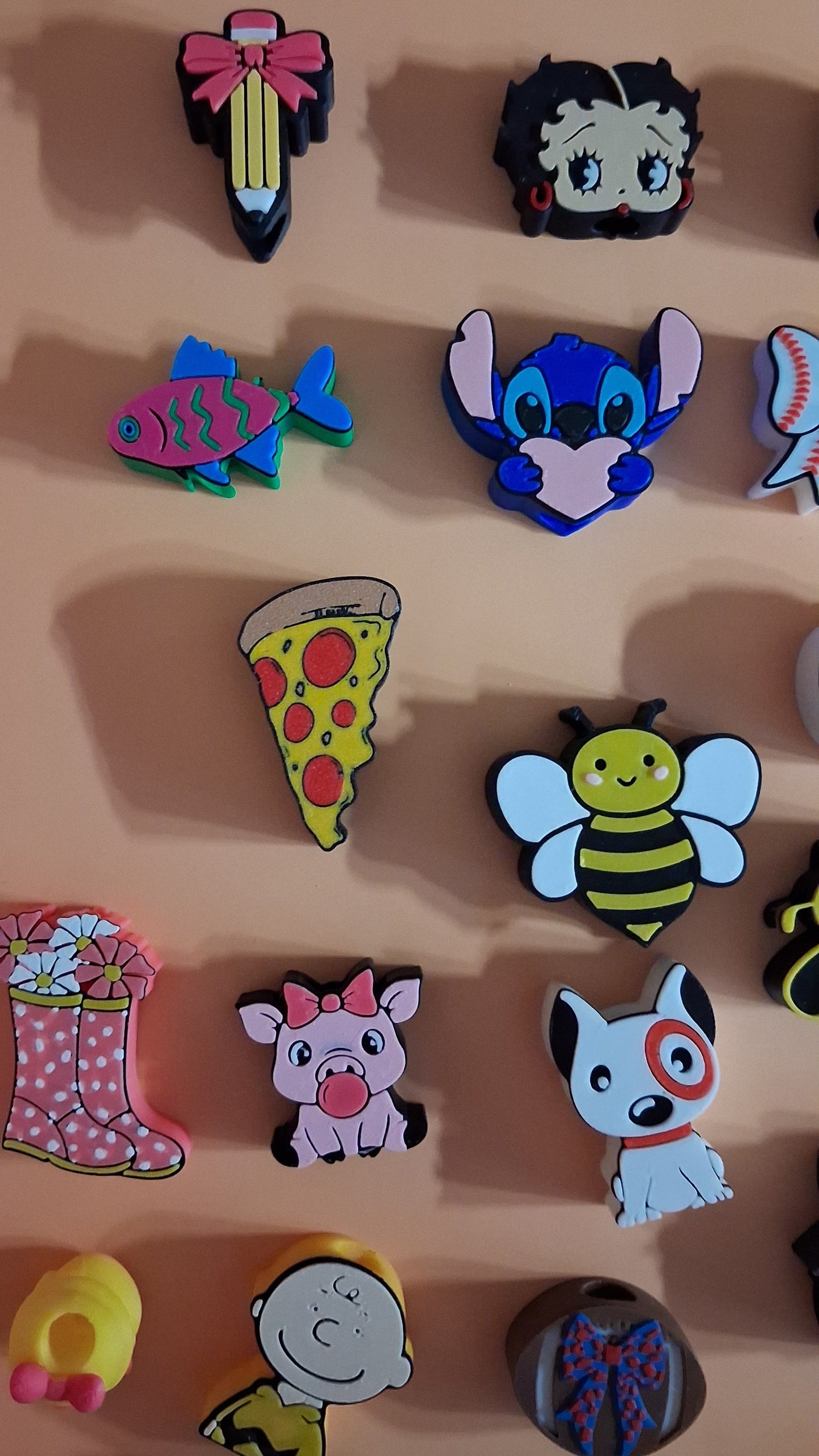 A collection of colorful, cartoon-themed straw toppers displayed on a beige surface. The charms feature various characters and objects, including a blue creature, a bee, a dog, a pizza slice, a pig, and a pink boot.