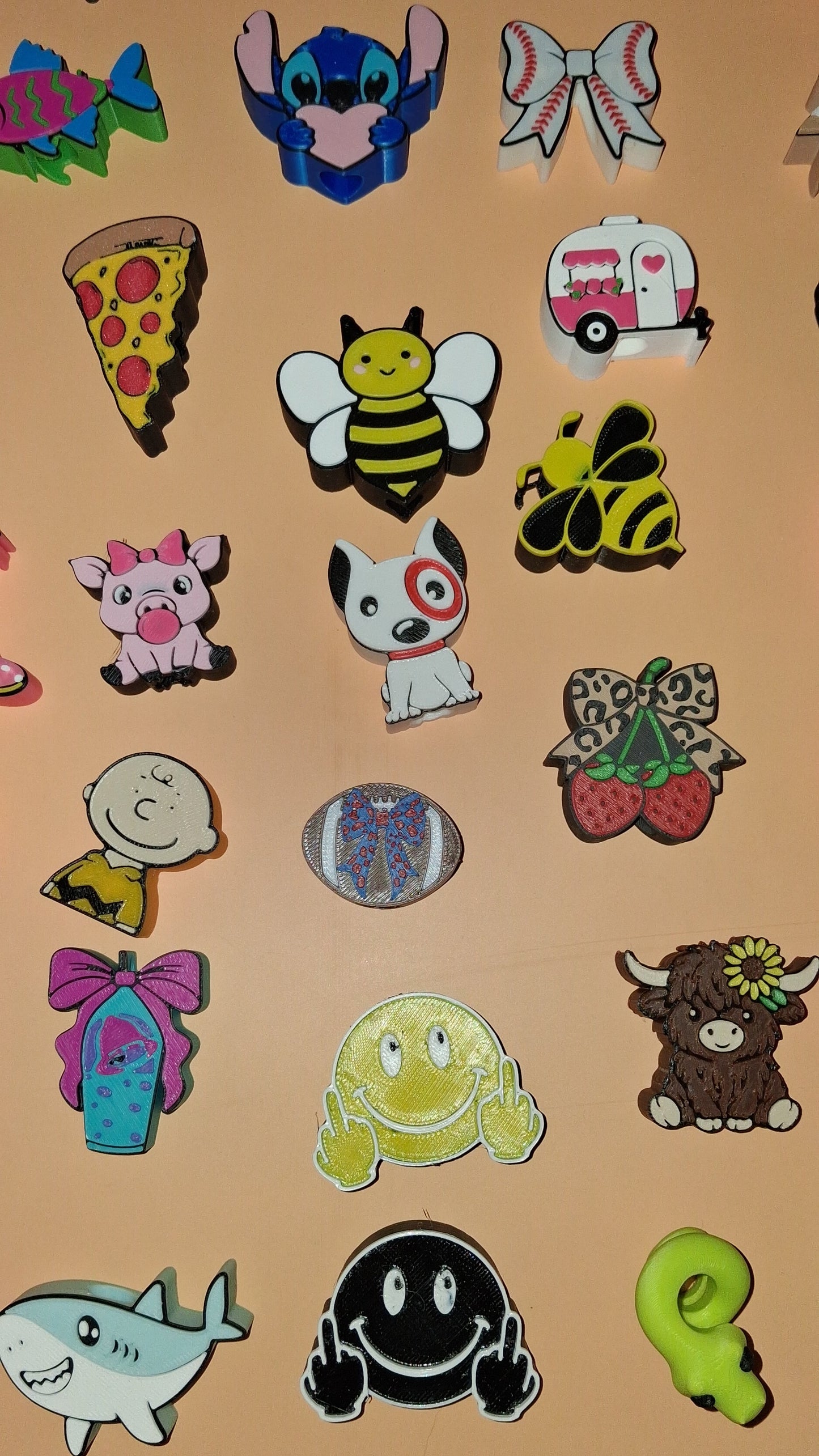 A collection of colorful cartoon straw toppers arranged on a plain beige background, including characters and objects like a bee, a pizza slice, a shark, a ghost, and animal motifs.