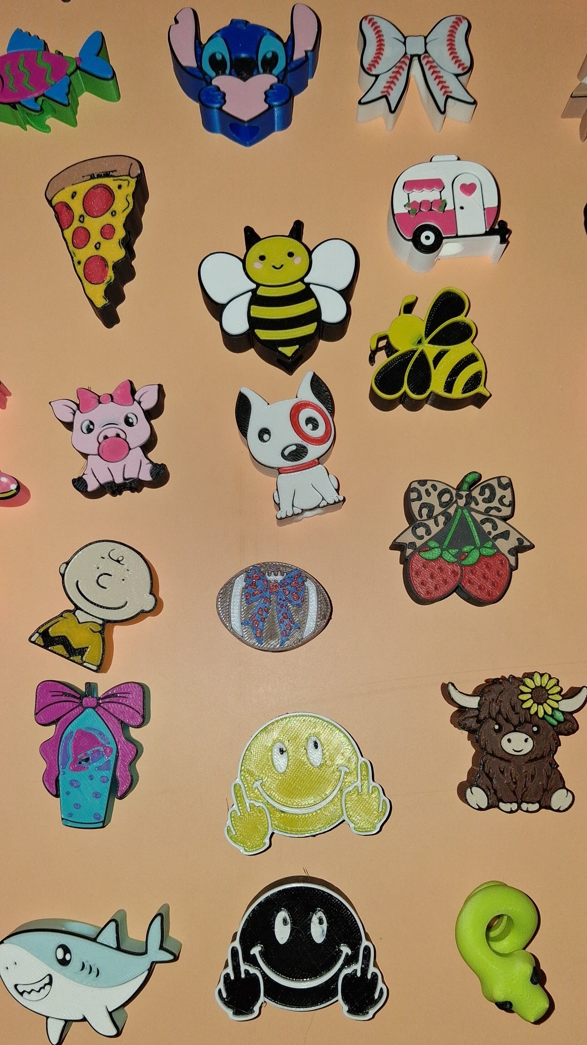 A collection of colorful cartoon straw toppers arranged on a plain beige background, including characters and objects like a bee, a pizza slice, a shark, a ghost, and animal motifs.